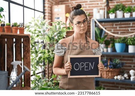 Hispanic woman working at florist holding open sign skeptic and nervous, frowning upset because of problem. negative person. 