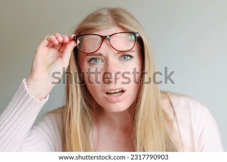 Shocked angry young woman in disbelief lowering glasses looking at camera with indignation isolated on grey blank studio background Royalty-Free Stock Photo #2317790903