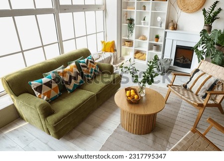 Interior of bright living room with cozy sofa, armchairs and coffee table near big window