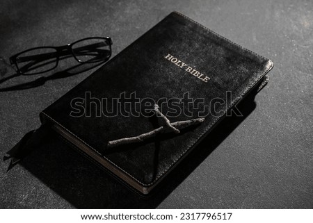Holy Bible with wooden cross and eyeglasses on black background