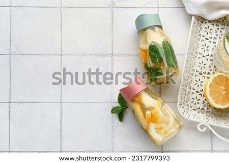 Sports bottles of infused water with lemon and mint on white tile background