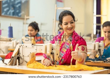 Indian women group showing thumbs up while work on sewing machine at textile factory.