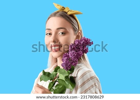 Young woman with lilac flowers on blue background, closeup