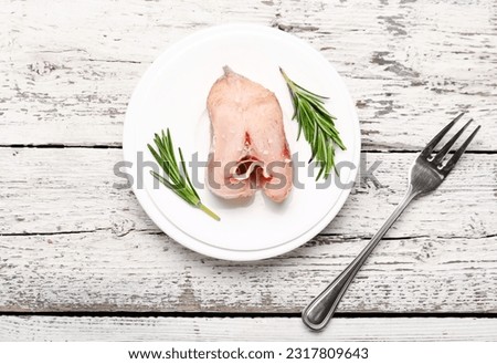 Plate with piece of raw codfish on light wooden background