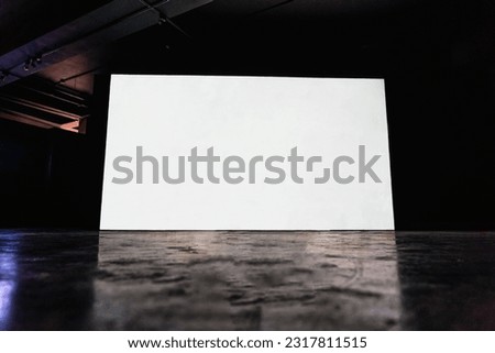 Empty room with blank mockup movie screen monitor standing in dark theater on black wall background. No people. Arts and entertainment concept.