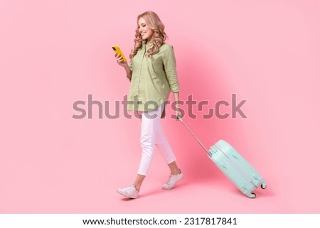 Full length photo of adorable sweet woman dressed green shirt walking holding luggage chatting device isolated pink color background