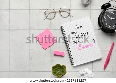 Notebook with question ARE YOU READY FOR EXAM?, alarm clock and eyeglasses on white tile background