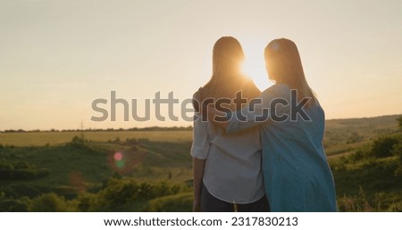 Mom hugs her teenage daughter, watching the sunset over a picturesque valley. Back view