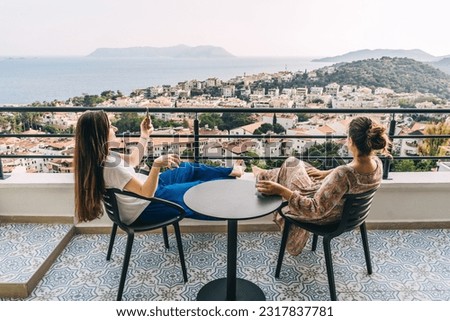 Two young girlfriends enjoy a beautiful view from the balcony of the city of Kas in Turkey at sunset.