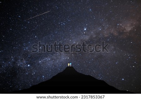 The Milky Way spreads out in the sky and shooting stars are flowing.
The back view of a couple looking up at the night sky from the summit.