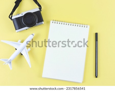 Top view or flat lay of blank page opened notebook with pen, airplane model and digital camera on yellow  background with copy space.