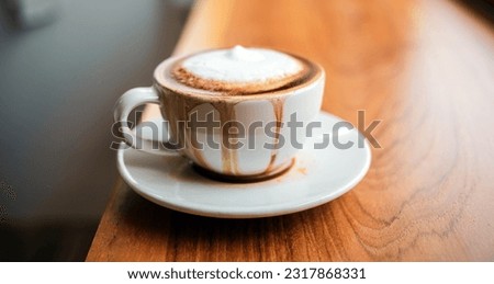 Spilled coffee with milk in a white cup or cappuccino is overflowing from the coffee cup on wooden bar Royalty-Free Stock Photo #2317868331