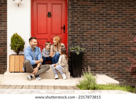 Family with a mother, father, son and daughter sitting outside on steps of a front porch of a brick house Royalty-Free Stock Photo #2317873815