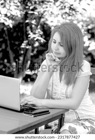 Black and white photo of a young woman working with a laptop in a summer cafe on the street. Coworking. Work outdoors. business concept