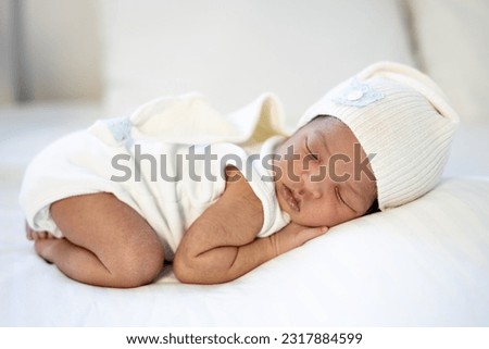 a newborn black African-American baby sleeps in a sleeping cap, a small dark-skinned baby lies on the bed in the bedroom on his tummy in close-up