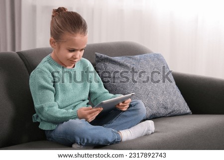 Little girl using tablet on sofa at home. Internet addiction