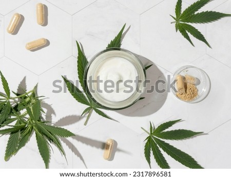 Cream jar and capsules with hemp protein powder near green cannabis leaves top view on a marble table, hard shadows. Organic healthcare and skincare products with CBD. Alternative medicine Royalty-Free Stock Photo #2317896581