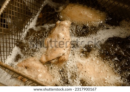 Cooking chicken wings in the deep fryer, boiling oil and fat in the deep fryer. Royalty-Free Stock Photo #2317900167
