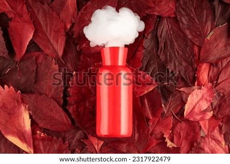 white smoke flies out of a red vase against a background of red leaves. puffs of white smoke and a vase, a genie from a bottle