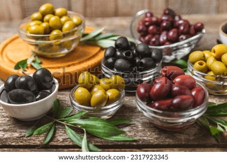 Green, black and red olives on a brown wooden background. Various types of olives in bowls and olive oil with fresh olive leaves. Copy space. Place for text. Mediterranean food. Vegan. Royalty-Free Stock Photo #2317923345