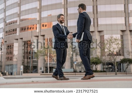 cheerful two business men handshaking. two business men handshaking outdoor. Royalty-Free Stock Photo #2317927521