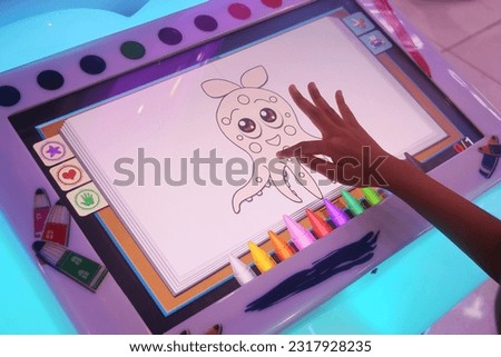 A small child is drawing and coloring a picture of squid using a game screen at the mall