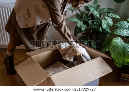 Cloth Donation. Woman sorting clothes at home to donate while decluttering closet, putting unwanted used clothing in cardboard box, wardrobe spring clean. Charity and volunteering Royalty-Free Stock Photo #2317929727