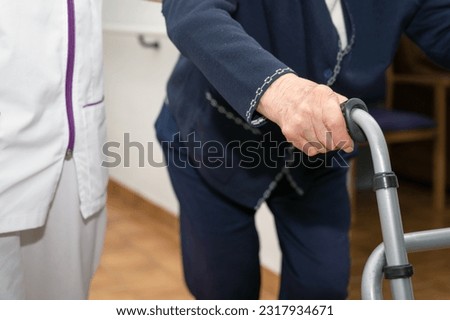 Nurse assists her senior patient on folding walker. Recuperation for elderly, seniors care, nursing home. High quality photo