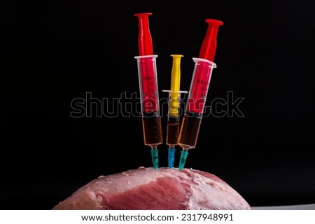 Injection from a syringe into raw meat on a dark background.Conceptual illustration of hormones and antibiotics in food production.