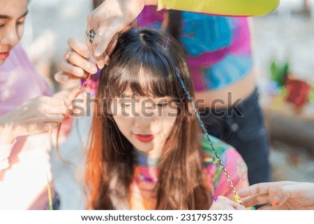 Girl makes stylish hairstyle with friends.
Outdoor Happy Asian friends preparation for a party in summer party.