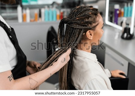 hair professional, tattooed beauty worker holding braids of female client in salon, beauty industry, salon job, customer in salon, hairdresser, salon services, hair make over Royalty-Free Stock Photo #2317955057
