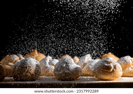 Baked profiteroles with custard cream on a wood plate sprinkled with powdered sugar