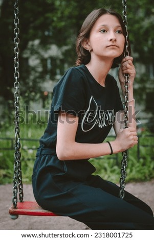A twelve year old girl is sitting on a swing in the playground. Summer photography. Child.