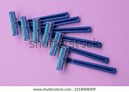 a set of six blue plastic razors lie on a pink table