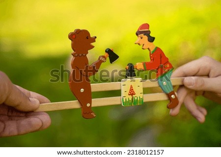 Vintage wooden children's toy in the hands of a child. The revival of toys of the last century.Wood painting.Craft toys.A man and a bear with axes.