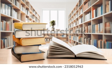 Book stack and opened book on the desk on blurred bookshelves in light public library room background