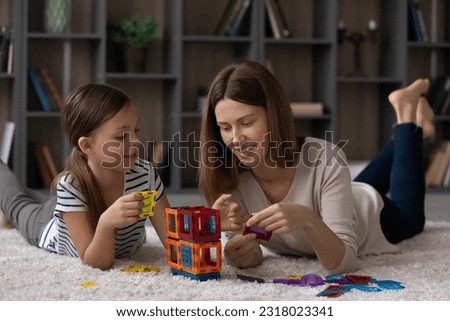 Happy mother and little daughter kid enjoying play on heating floor together, constructing plastic building or tower, completing toy house model, relaxing on carpet at home, enjoying playtime Royalty-Free Stock Photo #2318023341