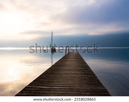 a wooden pier goes into the distance of the lake where the yacht stands against the backdrop of sunrise and mountains in the fog