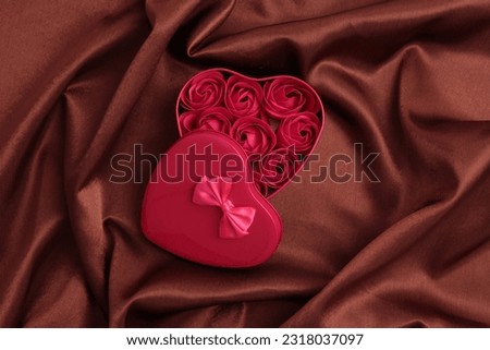 Heart frame gift box with rose flowers. Abstract brown pearl wave silk fabric texture background.