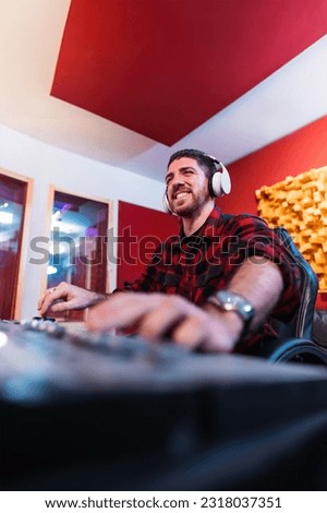 Vertical portrait of young sound engineer recording the audio and equalizing song in a professional music studio using computer wearing headphones. Happy man working on the master and mixing track