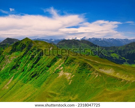 View on mountains near Saalbach Hinterglemm ski resort on a summer day,green meadows,mountains, blue sky, clouds, Hohen Tauern mountains with glaciers in background.  Alps, Austria. 