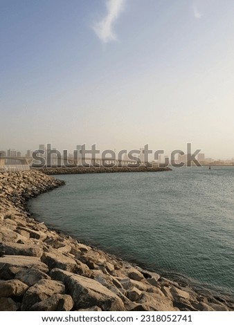 Large stones along the sea with a bridge and buildings in the background