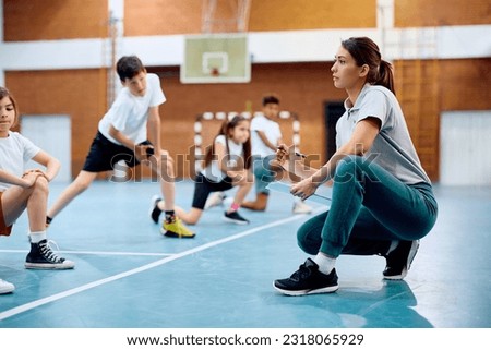 Young sports teacher talking to children during physical education class at school gym. 