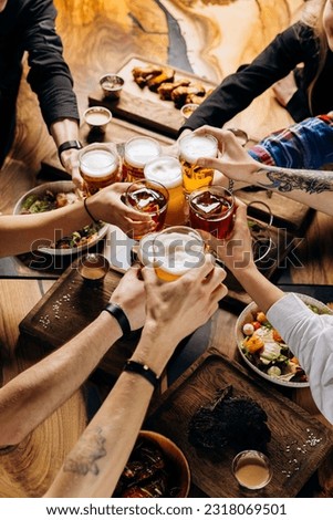 Friends cheering beer glasses on wooden table covered with delicious food - Top view of people having dinner party at bar restaurant - Food and beverage lifestyle concept Royalty-Free Stock Photo #2318069501