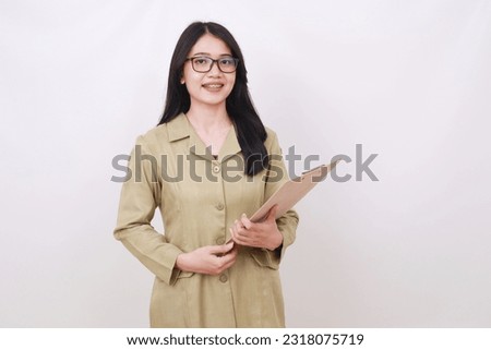 Pretty young Indonesian teacher standing while holding clipboard Royalty-Free Stock Photo #2318075719