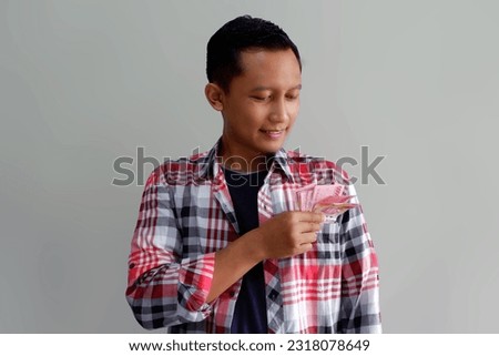 Adult Asian man smiling happy while putting paper money inside his shirt pocket