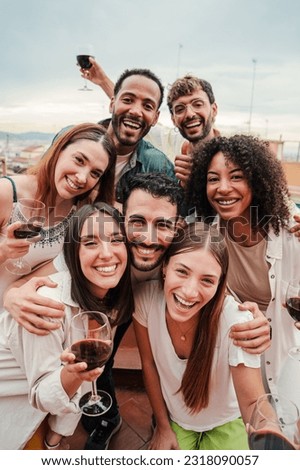 Vertical portrait. Group of best friends on a rooftop wine party. Young people drinking, toasting glasses, laughing and having fun on a friendly meeting, enjoying happy hour at winery bar restaurant