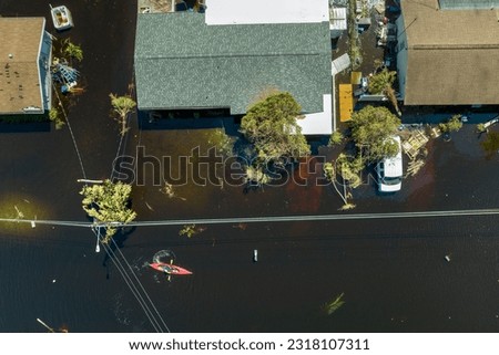 Aftermath of flooding natural disaster. Kayak boat floating on flooded street surrounded by hurricane Ian rainfall flood waters homes in Florida residential area Royalty-Free Stock Photo #2318107311