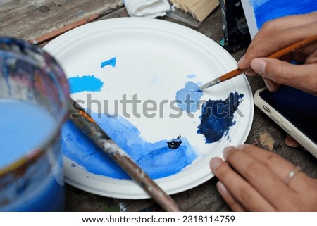 Close-up brush in hand, painter is using long-handled brush, mixing navy blue white together, In order lighten shade become bright blue, bright color paint color sky, mix slowly blend well.