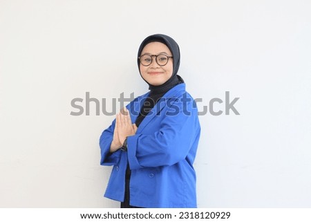 beautiful young Asian Muslim woman, wearing glasses and blue blazer with namaste gesture while smiling isolated white background.